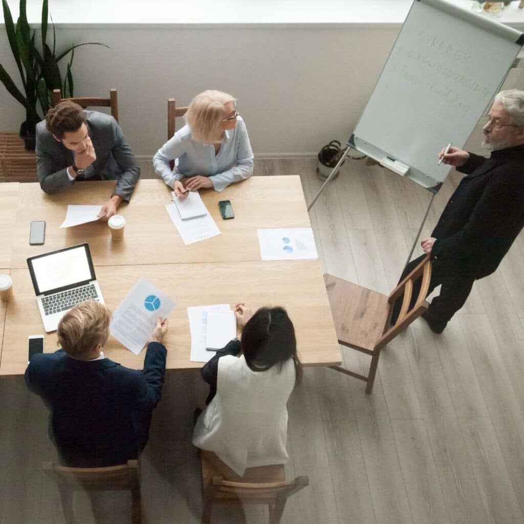 Eine Gruppe von Menschen sitzt am Schreibtisch und bekommt ein Führungskräfte-Coaching